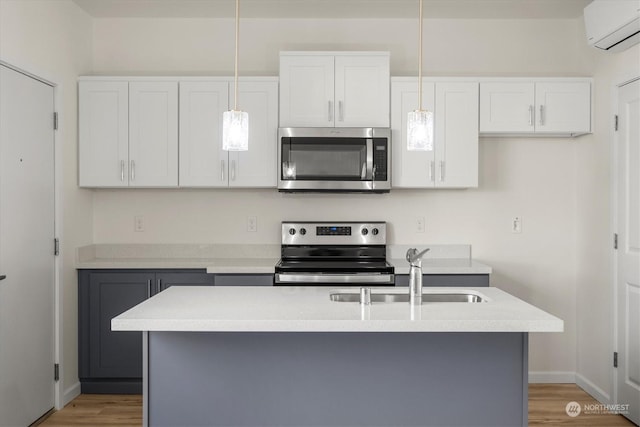kitchen with pendant lighting, sink, stainless steel appliances, white cabinets, and a center island with sink