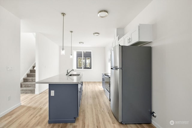 kitchen featuring pendant lighting, stainless steel refrigerator, an island with sink, sink, and range