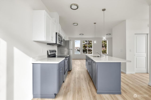 kitchen with sink, appliances with stainless steel finishes, a kitchen island with sink, white cabinets, and decorative light fixtures