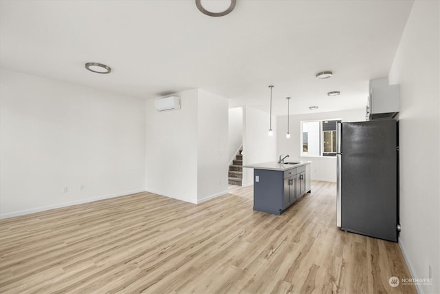 kitchen featuring sink, an AC wall unit, stainless steel refrigerator, pendant lighting, and a kitchen island with sink