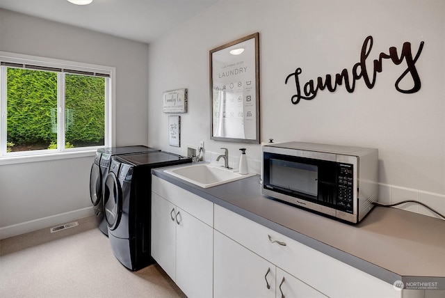 clothes washing area with washing machine and clothes dryer, cabinets, and sink