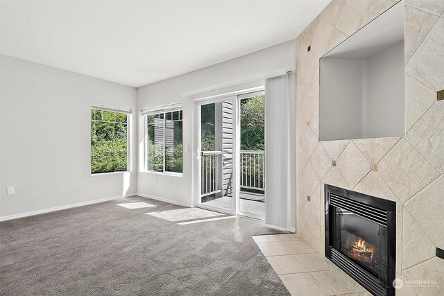 unfurnished living room featuring a tiled fireplace, light carpet, and a healthy amount of sunlight