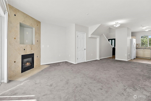 unfurnished living room featuring light colored carpet, a tiled fireplace, and sink