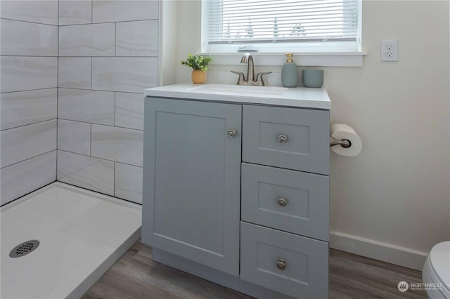 bathroom featuring a tile shower, vanity, wood-type flooring, and toilet