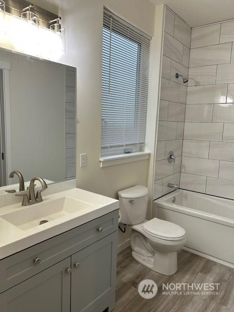 full bathroom featuring hardwood / wood-style flooring, tiled shower / bath combo, toilet, and vanity