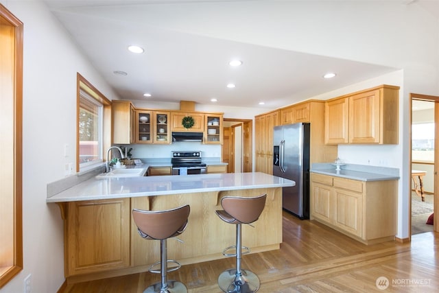 kitchen with appliances with stainless steel finishes, sink, a breakfast bar area, kitchen peninsula, and light hardwood / wood-style flooring