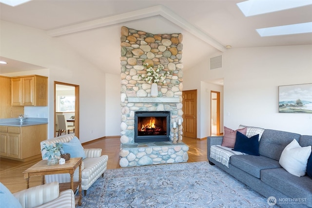 living room featuring beamed ceiling, a fireplace, a skylight, and high vaulted ceiling