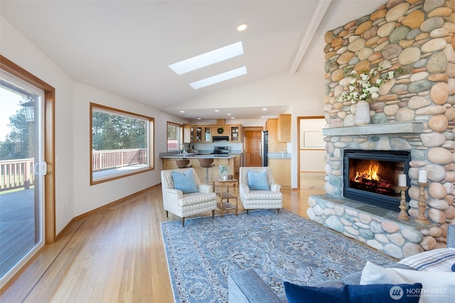 living room with light hardwood / wood-style flooring, a skylight, high vaulted ceiling, a fireplace, and beamed ceiling