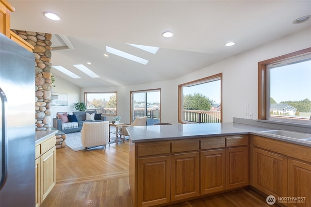 kitchen with lofted ceiling with skylight, sink, stainless steel refrigerator, and kitchen peninsula