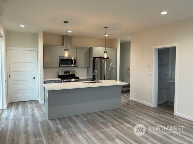 kitchen featuring gray cabinetry, sink, decorative light fixtures, a center island with sink, and appliances with stainless steel finishes