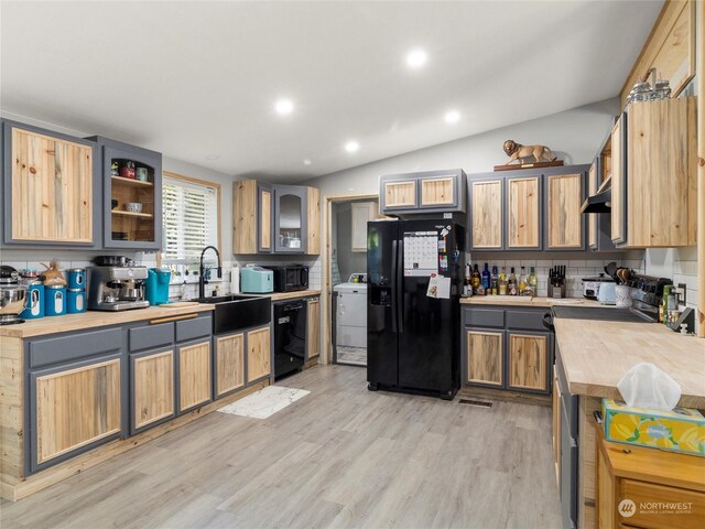 kitchen with light wood-type flooring, sink, black appliances, washer / clothes dryer, and lofted ceiling