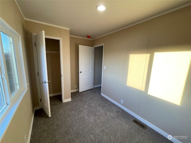 unfurnished bedroom featuring multiple windows, dark colored carpet, crown molding, and a closet