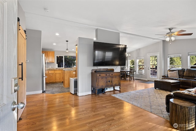 living room with hardwood / wood-style flooring, ceiling fan, a barn door, and vaulted ceiling