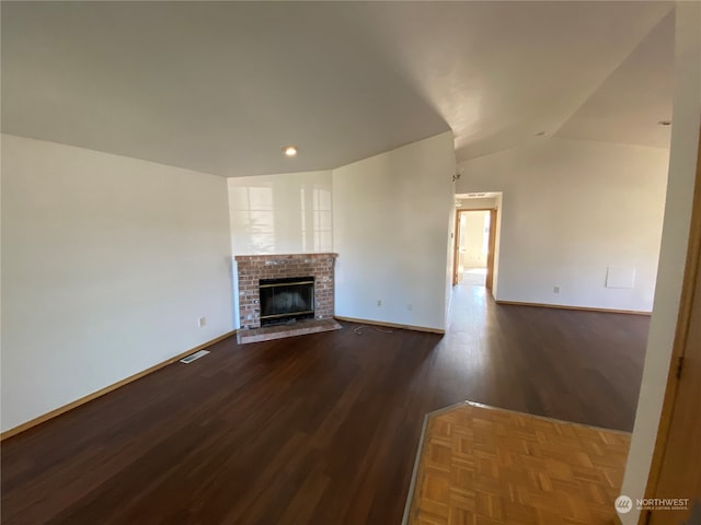 unfurnished living room with dark hardwood / wood-style flooring, a brick fireplace, and lofted ceiling