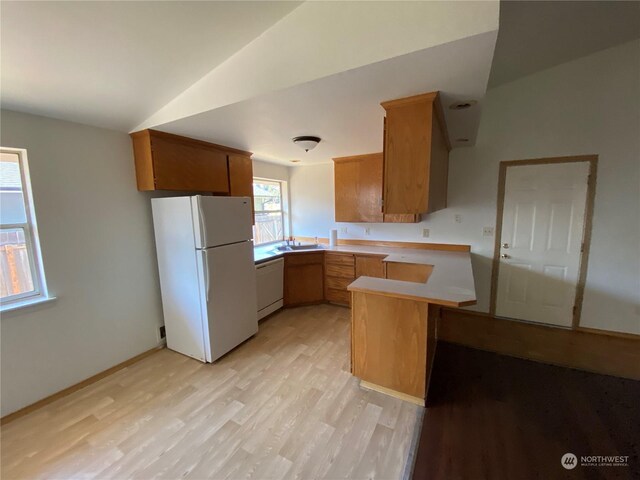 kitchen with white appliances, sink, kitchen peninsula, light wood-type flooring, and lofted ceiling