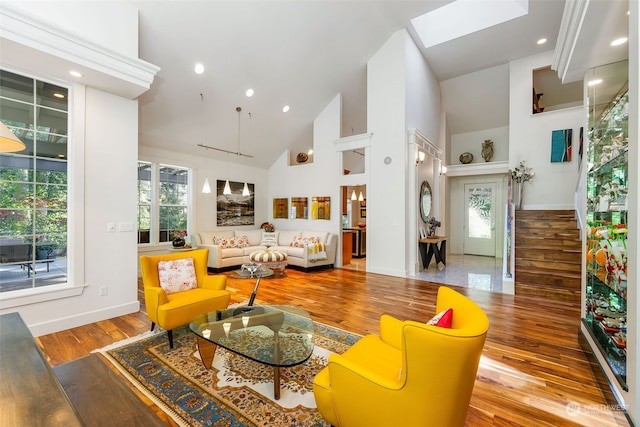 living area with a skylight, wood finished floors, high vaulted ceiling, baseboards, and stairs