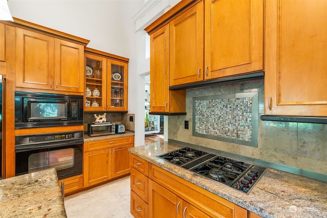 kitchen featuring black appliances, brown cabinetry, backsplash, and light stone countertops