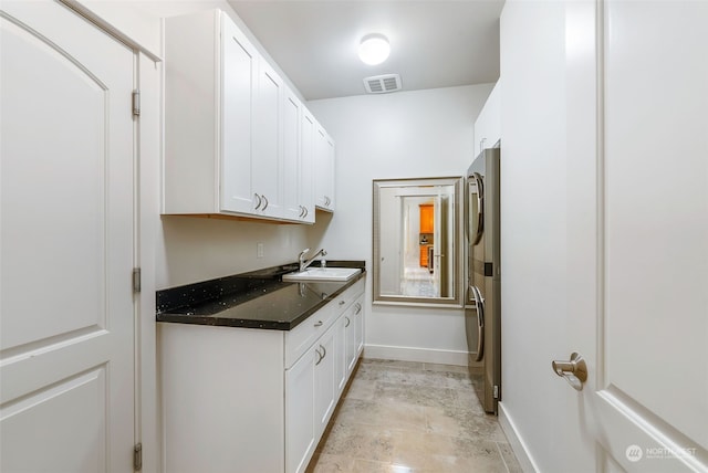 laundry area featuring sink, stacked washer and dryer, cabinets, and light tile patterned floors