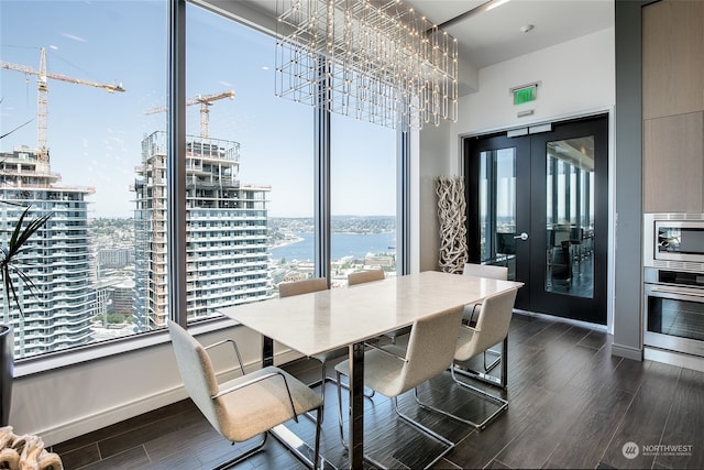 dining area featuring dark hardwood / wood-style flooring, a notable chandelier, french doors, and a water view