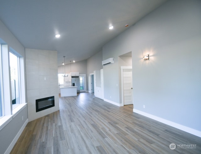 unfurnished living room with a wealth of natural light, a wall mounted air conditioner, a fireplace, and light hardwood / wood-style flooring