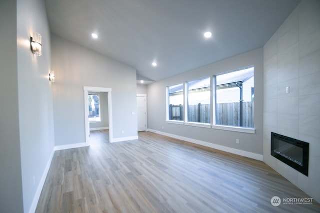 unfurnished living room featuring heating unit, vaulted ceiling, a tile fireplace, and light wood-type flooring