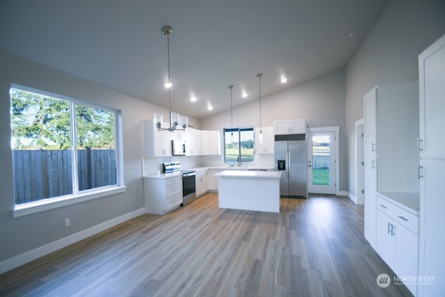 kitchen with a kitchen island, decorative light fixtures, white cabinets, stainless steel appliances, and light wood-type flooring