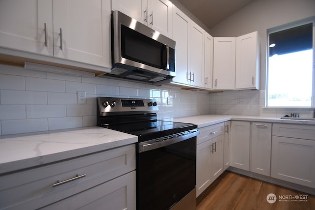 kitchen featuring stainless steel appliances, tasteful backsplash, light stone countertops, and white cabinets