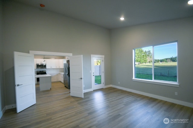 unfurnished bedroom with wood-type flooring, a towering ceiling, and stainless steel fridge