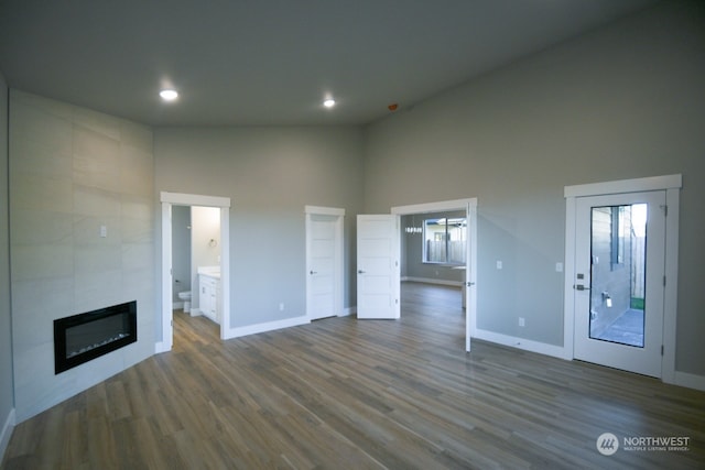 unfurnished living room featuring dark hardwood / wood-style flooring, a tiled fireplace, and a high ceiling