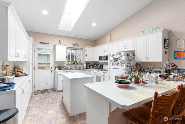 kitchen with white appliances, a breakfast bar, a skylight, a center island, and white cabinets