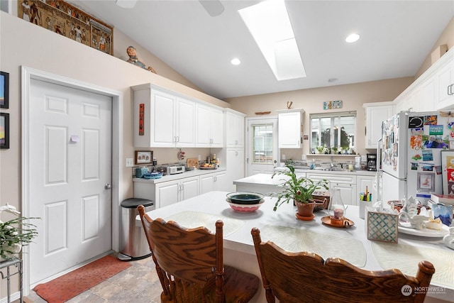 kitchen with white refrigerator, vaulted ceiling with skylight, and white cabinets