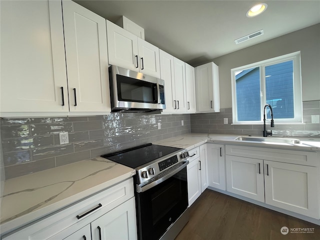 kitchen featuring light stone countertops, white cabinetry, dark wood-type flooring, stainless steel appliances, and backsplash