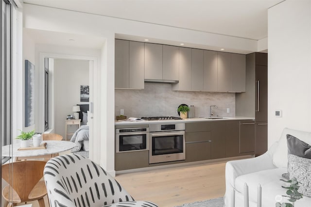 kitchen with sink, gray cabinetry, decorative backsplash, stainless steel appliances, and light wood-type flooring