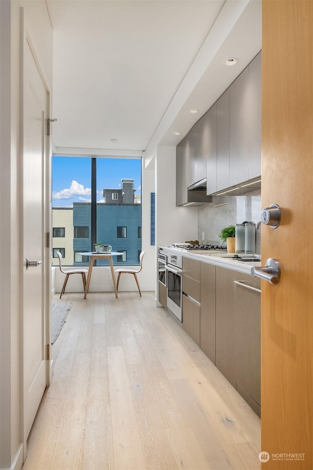 kitchen featuring decorative backsplash, light hardwood / wood-style flooring, oven, and expansive windows