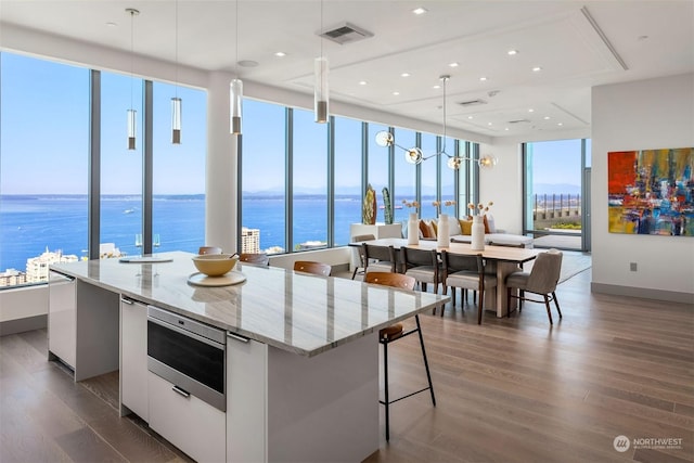 kitchen featuring white cabinetry, a water view, light stone counters, decorative light fixtures, and a large island with sink