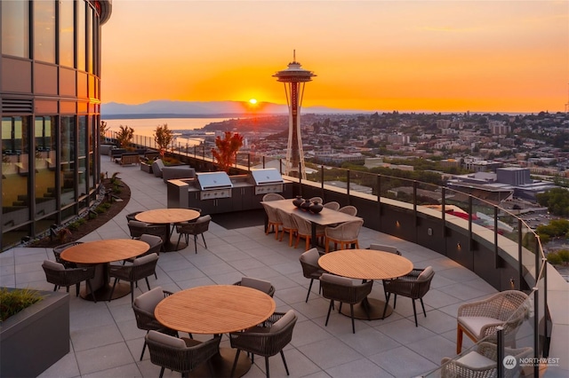 patio terrace at dusk with exterior kitchen, a water view, and area for grilling