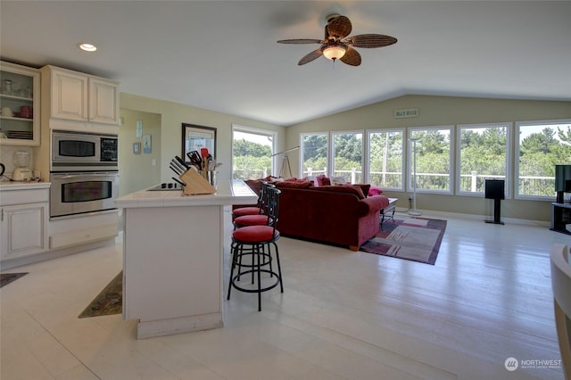 kitchen featuring a kitchen breakfast bar, ceiling fan, stainless steel appliances, lofted ceiling, and tile counters