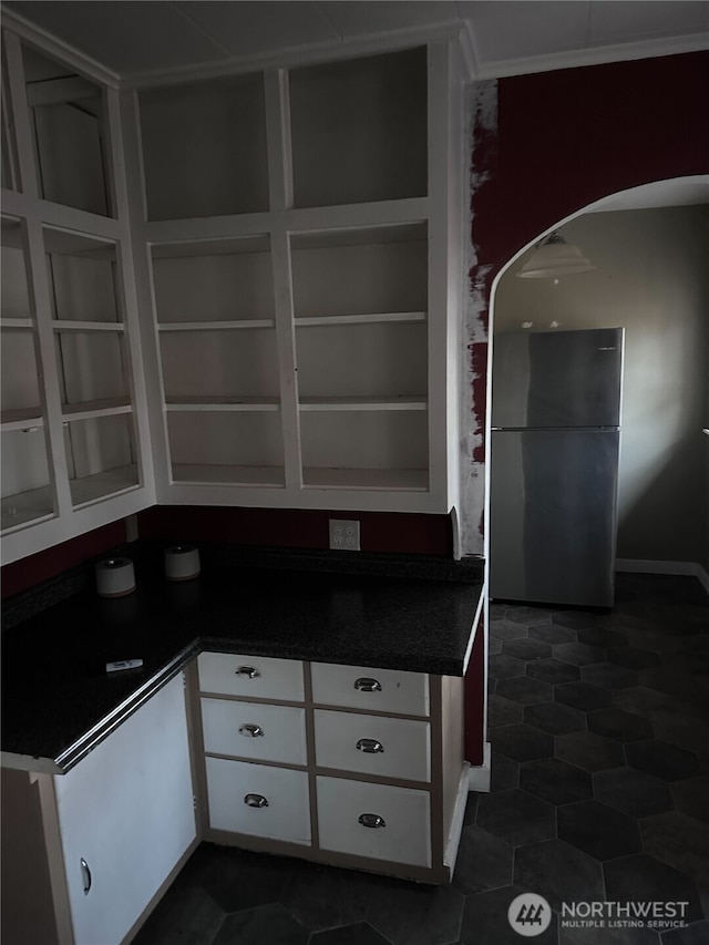 kitchen with dark countertops, white cabinets, arched walkways, and freestanding refrigerator