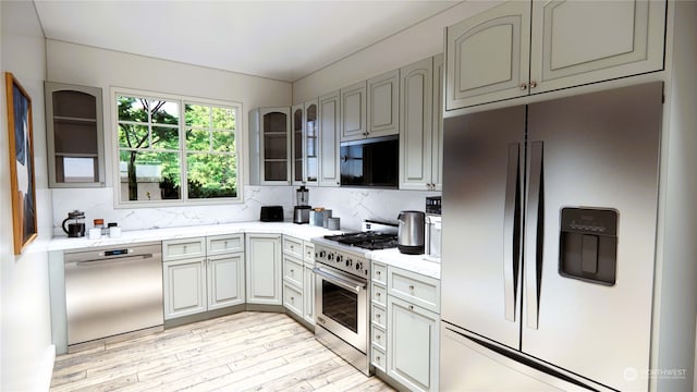 kitchen with decorative backsplash, light stone counters, stainless steel appliances, and light hardwood / wood-style floors