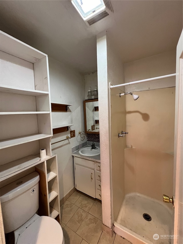 bathroom featuring vanity, a shower, a skylight, toilet, and tile patterned flooring