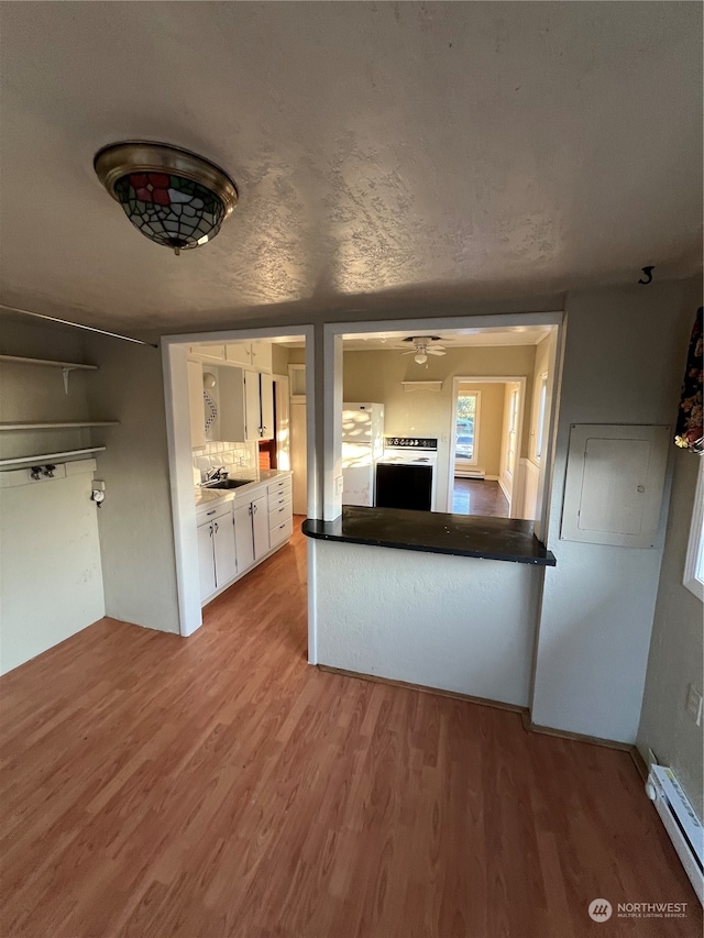 kitchen featuring white cabinetry, white fridge, baseboard heating, wood-type flooring, and sink