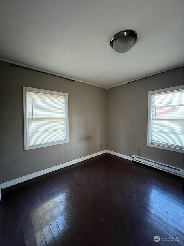 spare room featuring a baseboard heating unit, dark hardwood / wood-style flooring, and a wealth of natural light