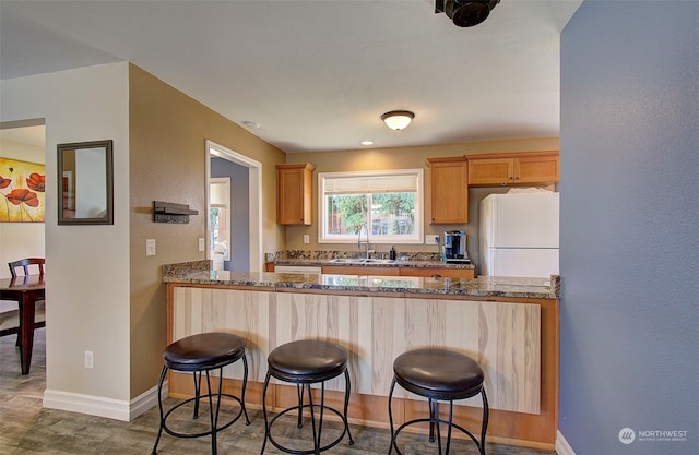 kitchen featuring sink, white fridge, dark stone counters, and a breakfast bar area