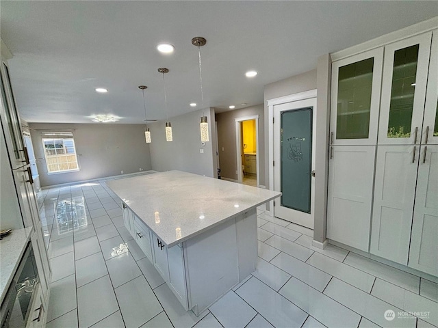 kitchen featuring light stone countertops, a center island, pendant lighting, and white cabinets