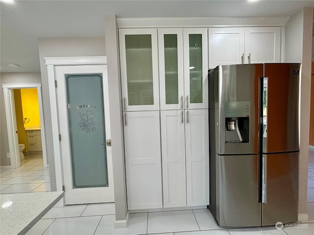 kitchen with stainless steel refrigerator with ice dispenser, light tile patterned floors, white cabinets, and light stone counters