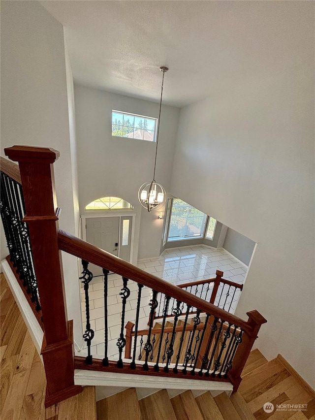 stairs with hardwood / wood-style flooring, a towering ceiling, and an inviting chandelier