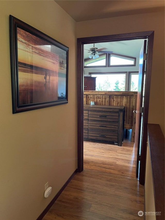 hallway featuring vaulted ceiling, light wood-style flooring, and baseboards