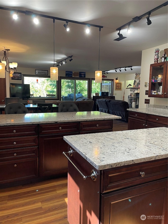 kitchen featuring decorative light fixtures, dark wood finished floors, glass insert cabinets, open floor plan, and light stone countertops