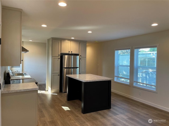 kitchen featuring gray cabinetry, dark hardwood / wood-style flooring, wall chimney range hood, and stainless steel refrigerator