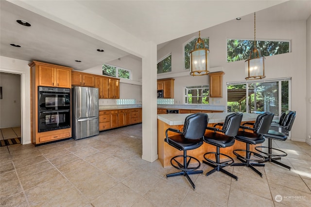 kitchen with light tile patterned floors, a kitchen breakfast bar, black double oven, stainless steel fridge, and high vaulted ceiling